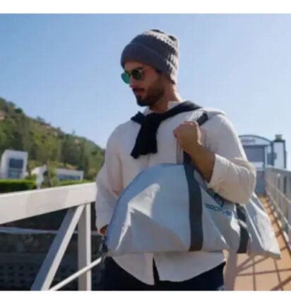 Man met zonnebril, grijze beanie, trui, draagt Epropulsion eLite buitenboordmotor dry bag, waterdicht bij steiger.