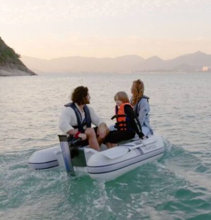 Drie opvarenden, soort met oranje reddingsvest, varen ePropulsion eLite elektrische buitenboordmotor rubberboot bij zonsondergang.