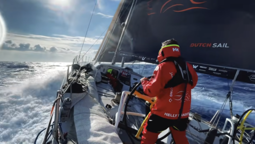 Zeiler in een Musto HPX-zeilpak (Gore-Tex) bestuurt een VO65 met nat dek en een „Dutch Sail“-grootzeil tijdens een oceaanoversteek op ruwe zee.